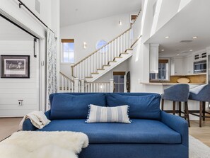 A modern living room with a blue sofa, a white fluffy rug, and a staircase leading to a kitchen area.