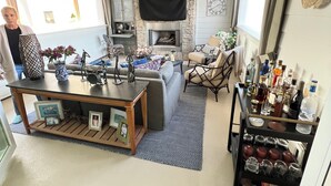 Una sala de estar acogedora con chimenea de piedra, un sofá, una mesa de centro con adornos y una estantería con varios objetos.