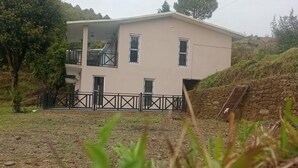 A two-story building with a balcony, surrounded by greenery and a stone wall.