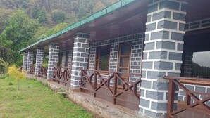 A row of stone buildings with a wooden balcony railing, set against a hillside backdrop.