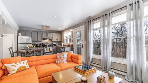 A modern living room with a sectional sofa, a coffee table, and a view of the kitchen and backyard. - Not-So-Tiny Tiny House with High-Speed Internet, 60-inch TV, Deck, and More! (Galena)