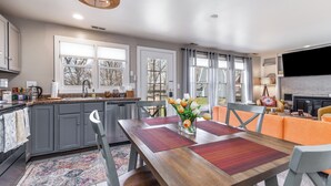 A modern kitchen with grey cabinets, a wooden dining table, and a large window. - Not-So-Tiny Tiny House with High-Speed Internet, 60-inch TV, Deck, and More! (Galena)