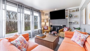 A living room with orange sofas, a coffee table, a fireplace, and a TV mounted on the wall. - Not-So-Tiny Tiny House with High-Speed Internet, 60-inch TV, Deck, and More! (Galena)
