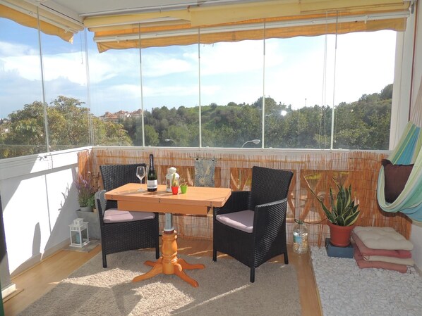 A balcony with a table, two chairs, a bottle of wine, and potted plants.