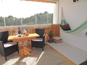 A balcony with a wooden table, wicker chairs, a hammock, and a view of greenery.