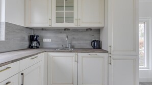 A kitchen with white cabinets, a grey backsplash, and a window providing natural light. - Modern, Cosy Family Bungalow Near Beach (Sint Maartensbrug)