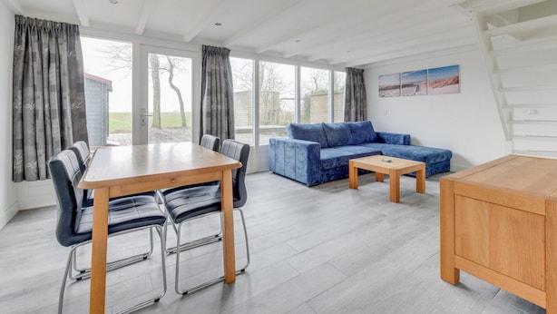 A modern living room with a wooden dining table, blue sofa, and a small coffee table. - Modern, Cosy Family Bungalow Near Beach (Sint Maartensbrug)