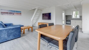 A modern living room with a blue sofa, a wooden dining table, and a staircase leading to another level. - Modern, Cosy Family Bungalow Near Beach (Sint Maartensbrug)