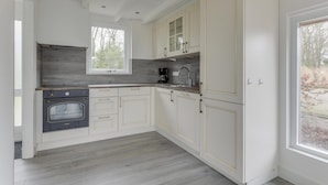 A modern kitchen with white cabinetry, a built-in oven, and a window providing natural light. - Modern, Cosy Family Bungalow Near Beach (Sint Maartensbrug)