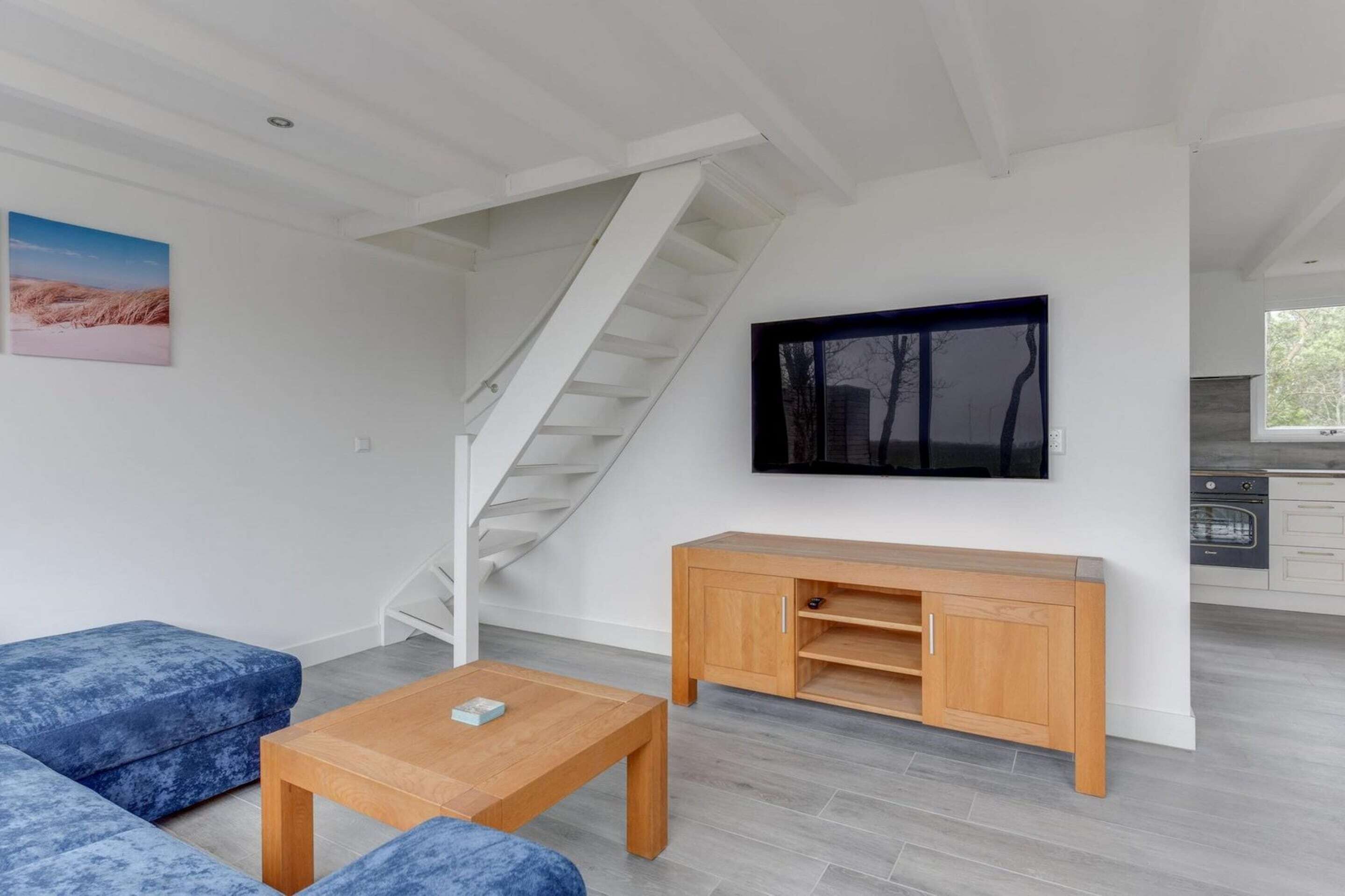 A modern living room with a staircase, a wooden cabinet, a blue sofa, and a television.