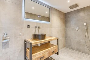 Une salle de bain moderne avec un meuble-lavabo en bois, un évier en acier inoxydable, un miroir et un espace douche.