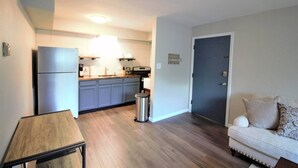 A compact kitchen with a refrigerator, sink, and stove. There is a trash can and a small table. The room has light-colored walls and wooden flooring. - Oak Overflight Oasis Condo-Minutes to WPAFB & WSU with AC, fast WiFi (Fairborn)