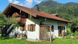 A traditional wooden house with a sloped roof, a wooden staircase, and a stone wall.