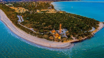 An aerial view of a coastal area with a lighthouse, clear blue waters, and a sandy beach.