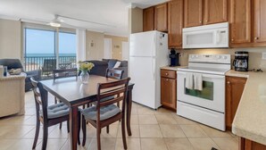 A kitchen with wooden cabinets, a refrigerator, a microwave, an oven, and a dining table with chairs. - GULF VIEW | 2 QUEEN BEDS | SLEEPS 4 | 5TH FLOOR BALCONY | STEPS TO BONITA BEACH (Bonita Springs)