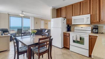 A kitchen with wooden cabinets, a refrigerator, a microwave, an oven, and a dining table with chairs.