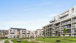 A modern apartment complex with multiple balconies, a central courtyard with a water feature, and a well-maintained lawn. - Sea En Rose - family stay near beach and centre (Oostende)