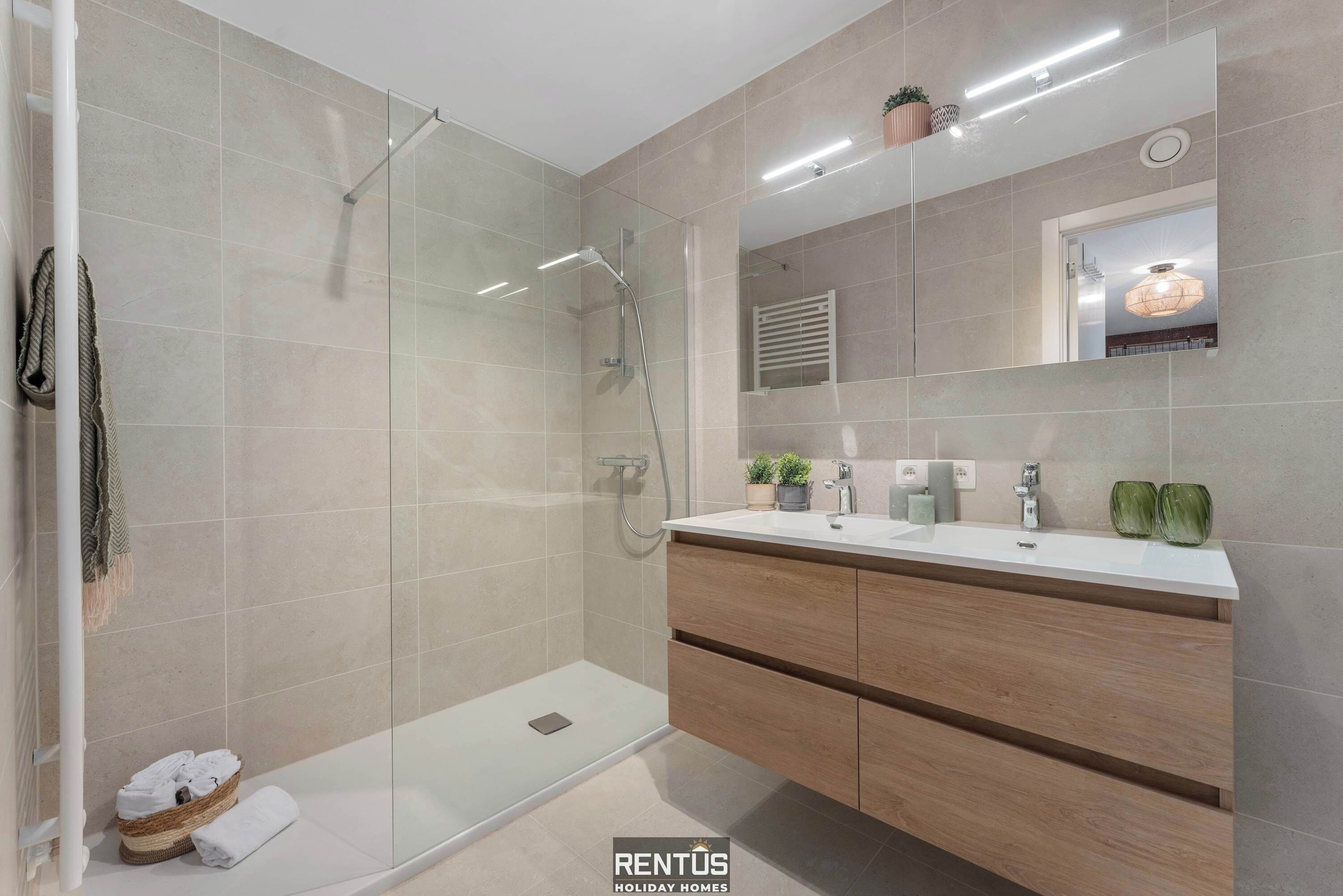 A modern bathroom with a glass-enclosed shower, a wooden vanity with a mirror, and a tiled floor.