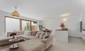 A modern living room with a sectional sofa, a dining area, and a kitchen.