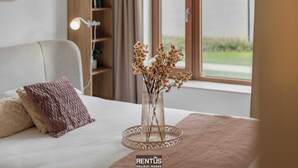 A bedroom with a bed, a bedside table, a lamp, a bookshelf, and a window with a view of greenery. - Sea En Rose - family stay near beach and centre (Oostende)