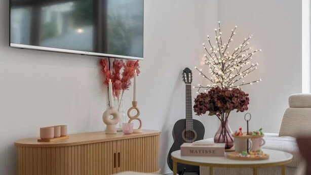 A modern living room with a wooden cabinet, a guitar, a TV mounted on the wall, and a round table with a book titled "MATISSE". - Sea En Rose - family stay near beach and centre (Oostende)