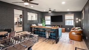 A modern living room with a foosball table, a bar area, and a comfortable seating arrangement. - The Dunn Right - Pool, Game Room, Yard Games, 1.5 Miles to TAMU (Bryan)