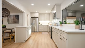 A modern kitchen with white cabinetry, stainless steel appliances, and a wooden dining table. - The Dunn Right - Pool, Game Room, Yard Games, 1.5 Miles to TAMU (Bryan)