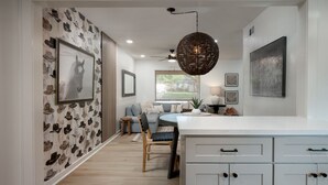 A modern kitchen with white cabinetry, a central island, and a dining area with a sofa and chairs. - The Dunn Right - Pool, Game Room, Yard Games, 1.5 Miles to TAMU (Bryan)