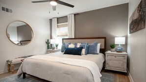 A bedroom with a bed, bedside tables, a ceiling fan, a mirror, and a window with curtains. - The Dunn Right - Pool, Game Room, Yard Games, 1.5 Miles to TAMU (Bryan)