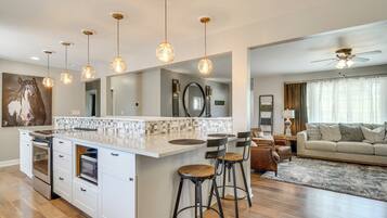 Une cuisine moderne dotée d’un îlot central, de tabourets de bar, de luminaires suspendus et d’un coin repas avec un canapé et des rideaux.