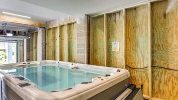 A hot tub in a room with wooden paneling and a visible electrical outlet.