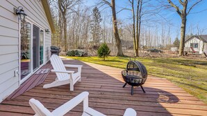 A wooden deck with white chairs and a fire pit, surrounded by trees and a grassy yard. - 3 Mi to Duck Lake State Park: Home w/ Deck! (Muskegon)