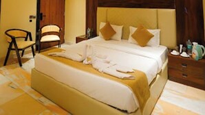 Una habitación de hotel con una cama grande, un ventilador de techo, un cabecero de madera y una mesita de noche con lámpara.