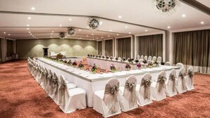 Un amplio salón de conferencias con una larga mesa, sillas decoradas con lazos y una araña.