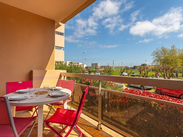 A balcony with a table set for dining, overlooking a parking area and buildings. - L'Alicastre by Interhome (Le Lavandou)