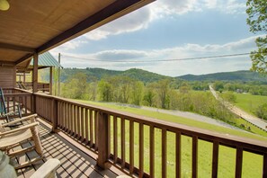 A wooden deck with a view of a green valley and a road.