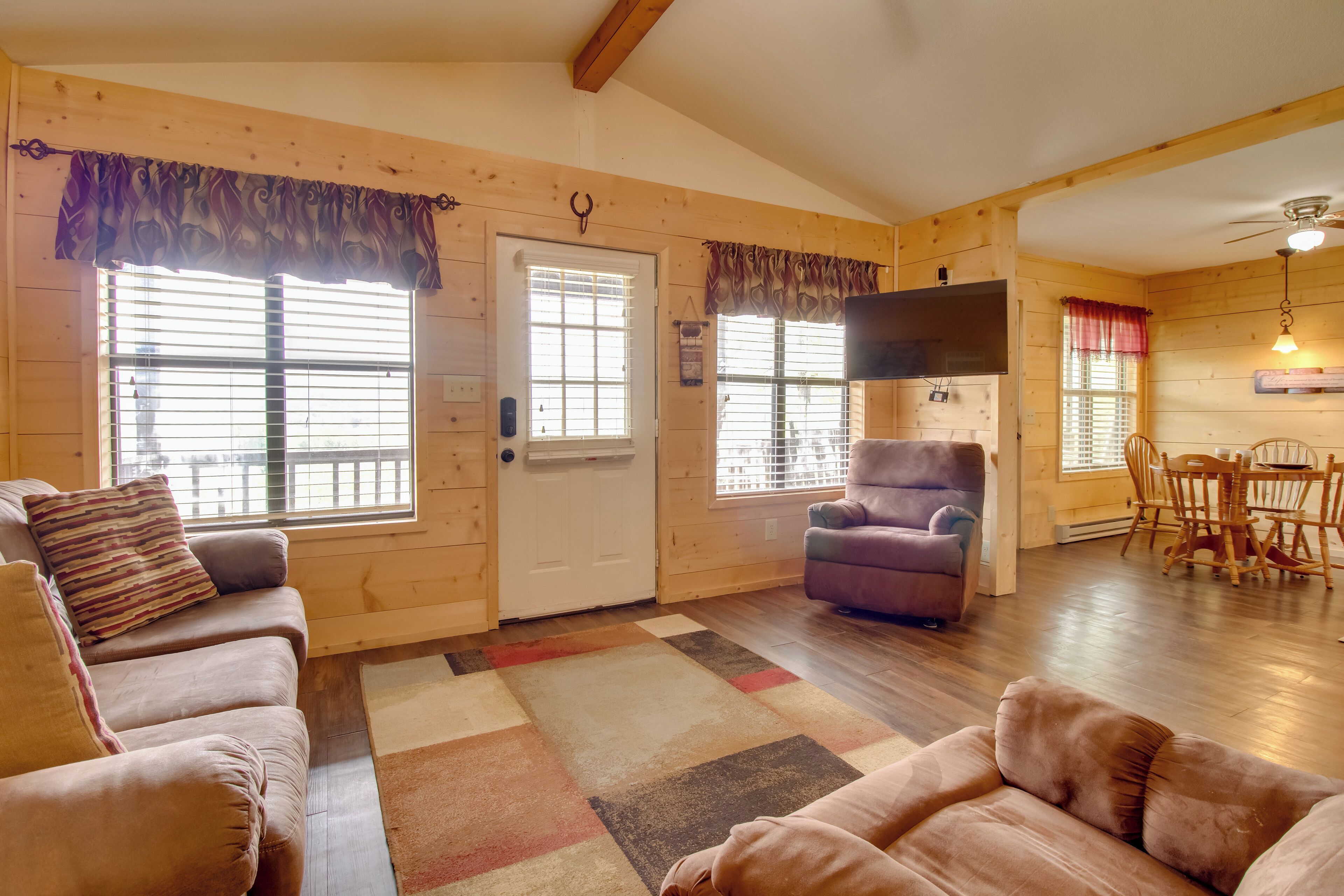 A cozy cabin interior with a wooden interior, a sofa, a chair, and a dining area.