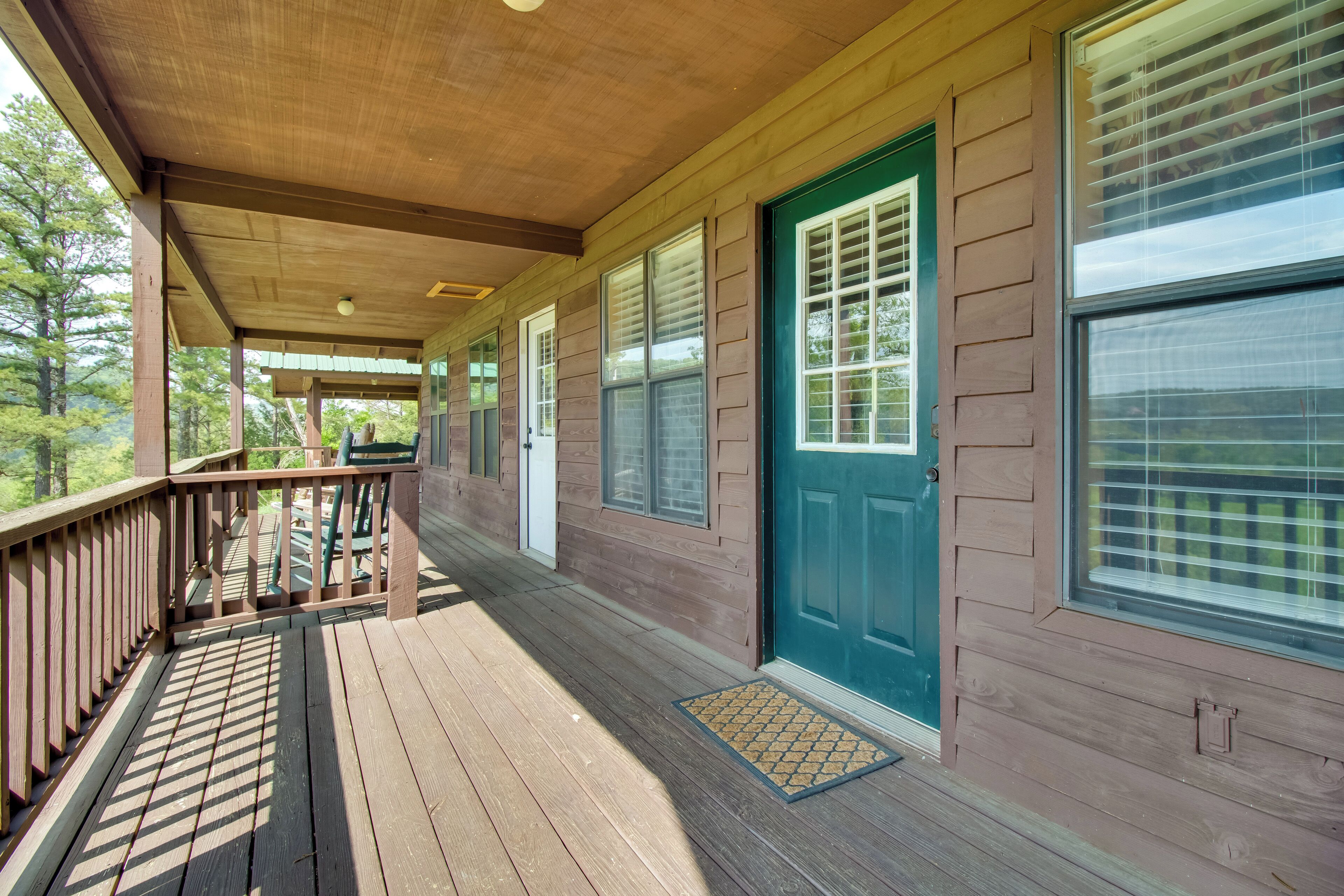 A covered wooden deck with a green door and windows, overlooking a forested area.