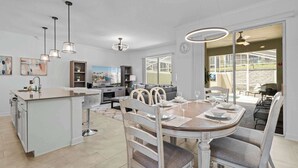A modern kitchen with a central island, dining area with a round table and chairs, and a view of the outdoor patio. - Magical Themed Home with Pool in Top Resort (Davenport)