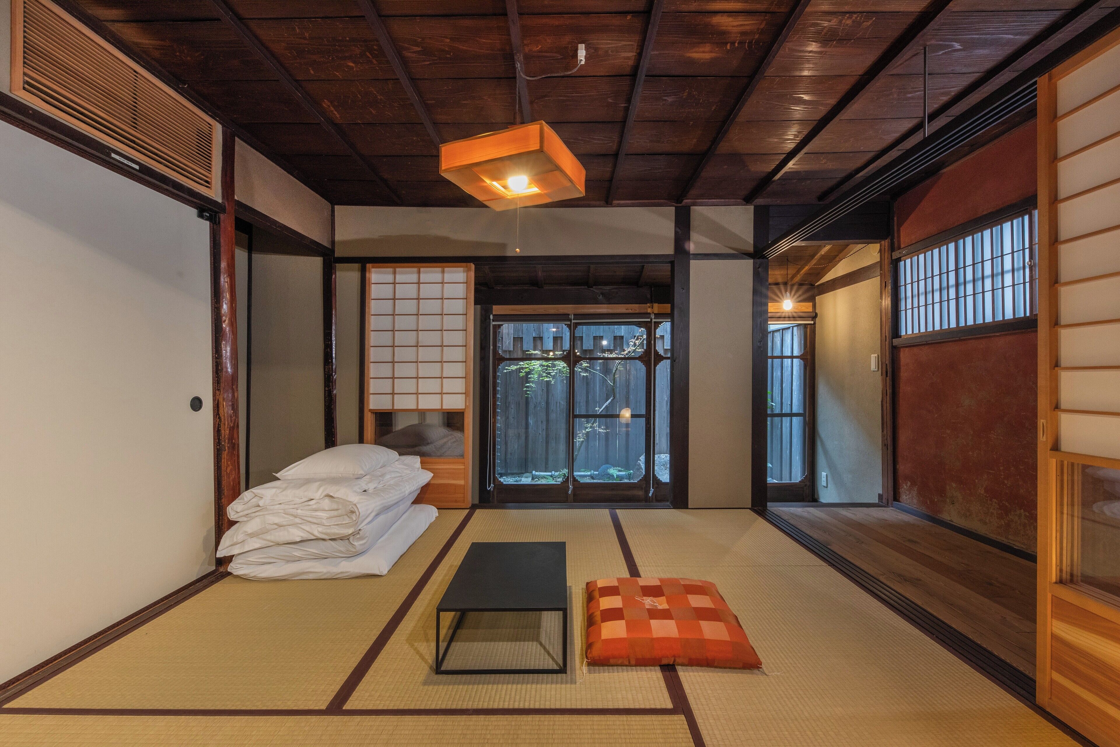 A traditional Japanese room with tatami flooring, a futon bed, a black table, and a sliding door leading to a garden.