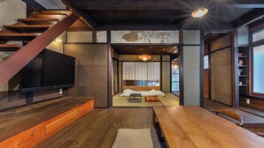 A traditional Japanese-style room with tatami flooring, a low wooden table, a television, and a sliding door leading to a tatami room.