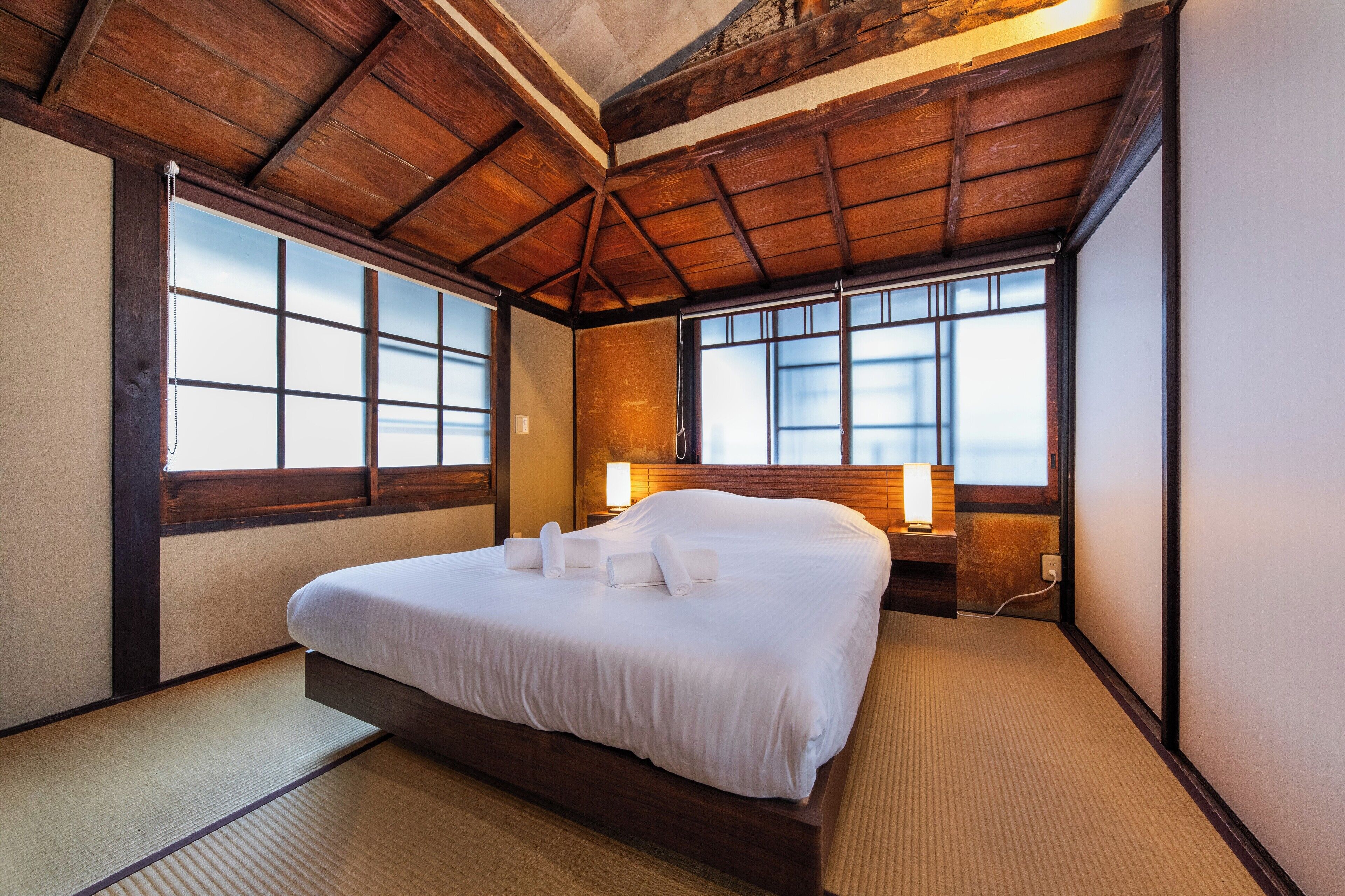 Ein traditioneller japanischer Raum mit Tatami-Böden, einem großen Bett mit weißer Bettwäsche und Holzbalken an der Decke.