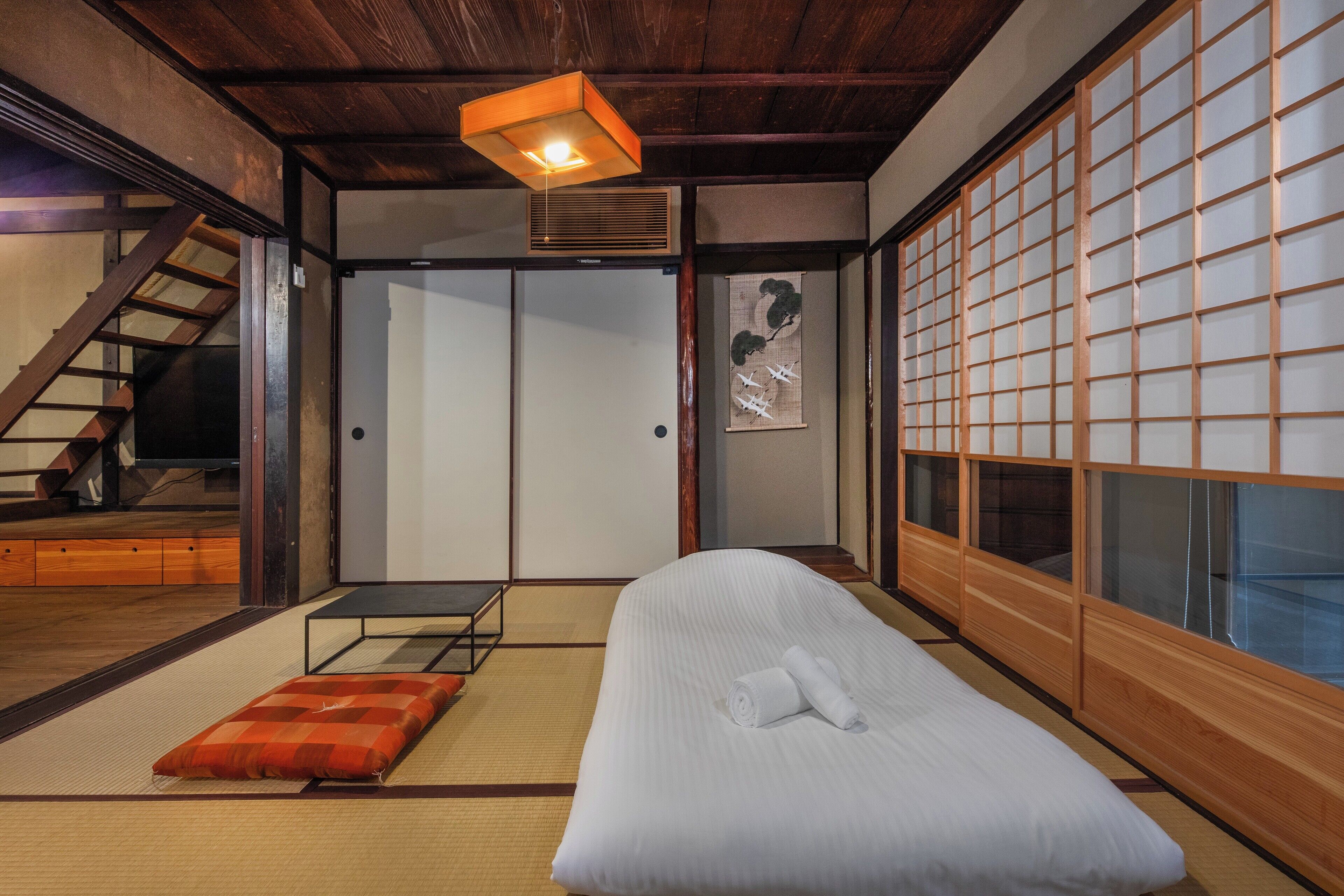 A traditional Japanese room with tatami flooring, a futon bed, sliding doors, and a wooden staircase.