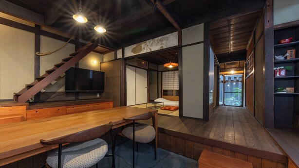 A traditional Japanese-style room with a wooden dining table, chairs, a television, and a view of the outside.