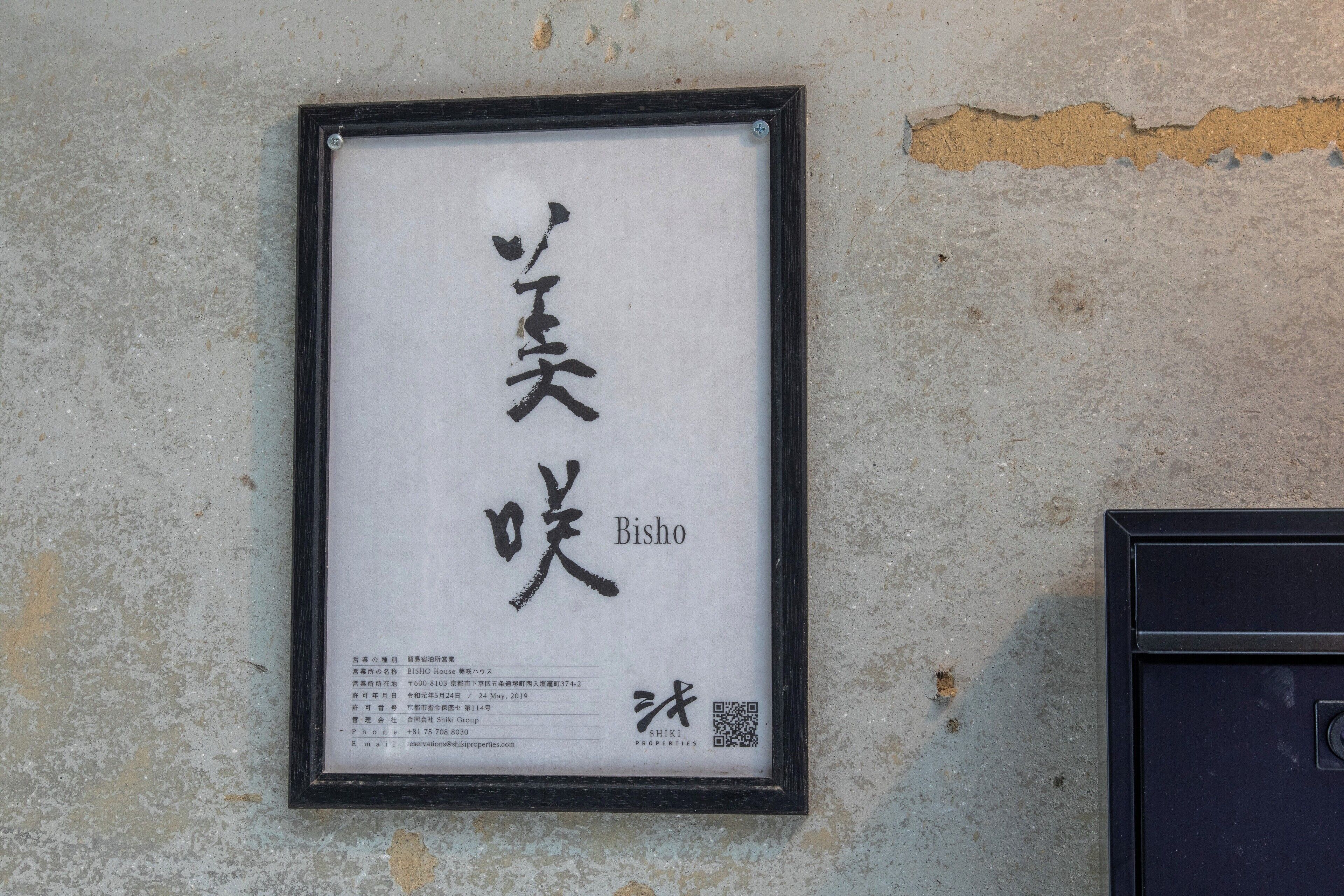 Un letrero enmarcado con caracteres japoneses y la palabra 'Bisho' sobre una pared con textura.