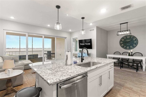 A modern kitchen with a marble countertop, stainless steel appliances, and a dining area with a white table and chairs.