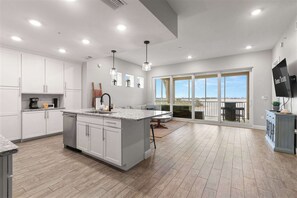 A modern kitchen with a large island, white cabinetry, and a dining area with a view.