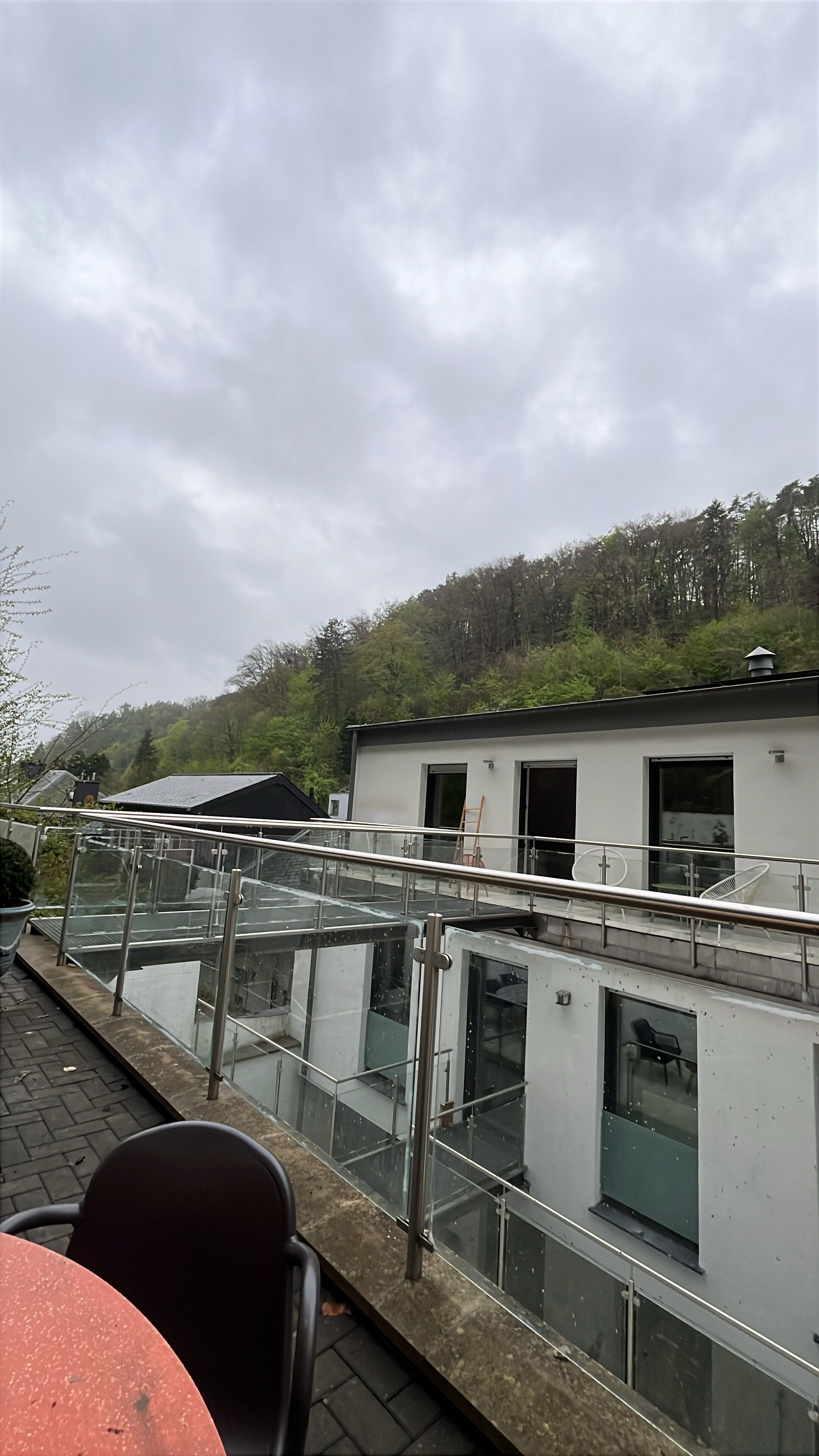 Un bâtiment moderne doté d’un balcon en verre, d’une table rouge et de chaises.