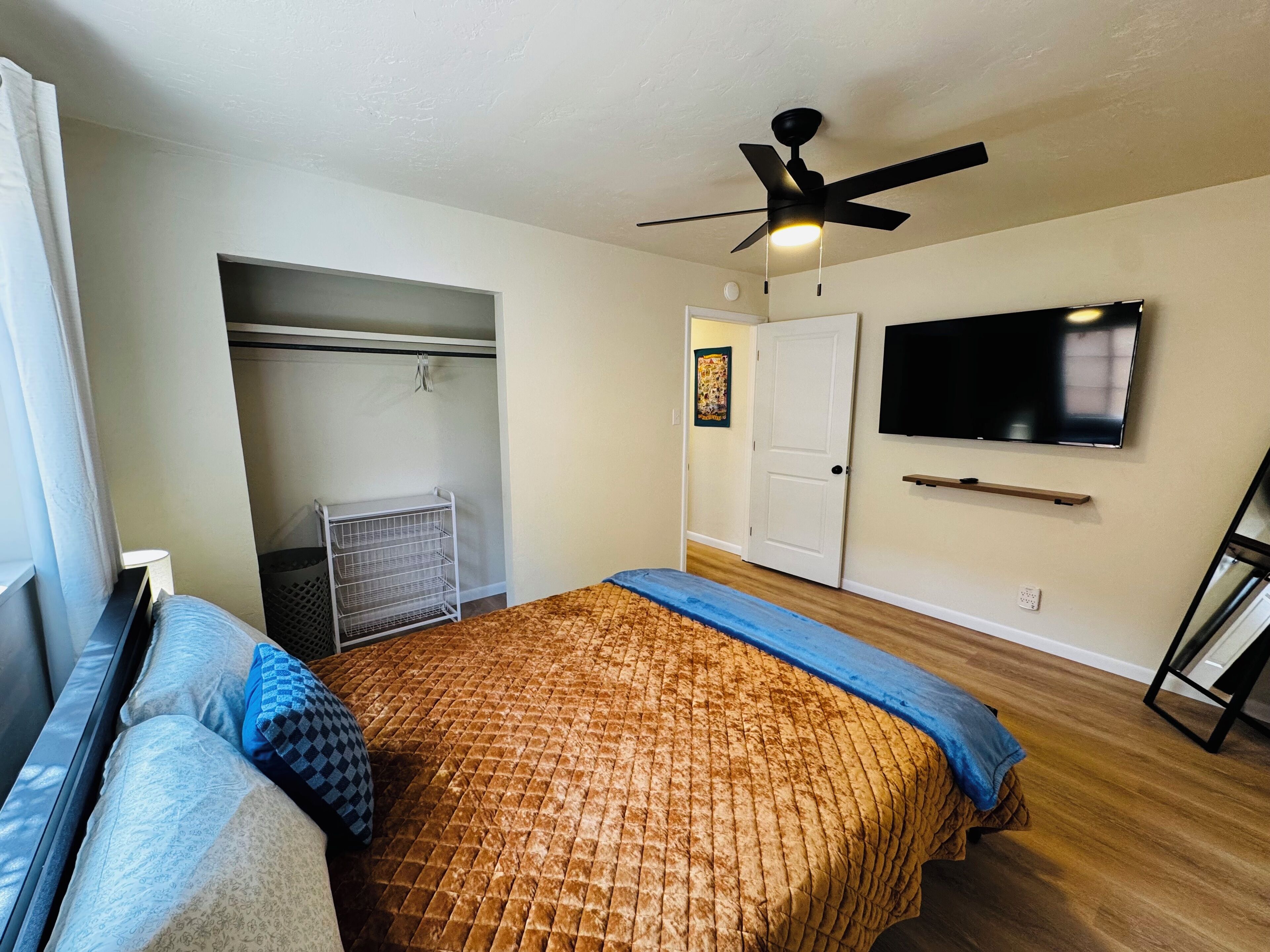 Une chambre à coucher avec un lit, un ventilateur de plafond, une télévision, une armoire et une porte.