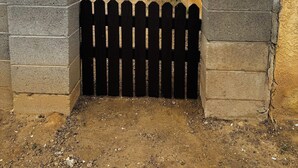 A fenced outdoor area with a dirt ground, a wooden fence, and a building with a yellow wall. - Free Chick-fil-A & Starbucks! 502 Hideaway! (Farmington)